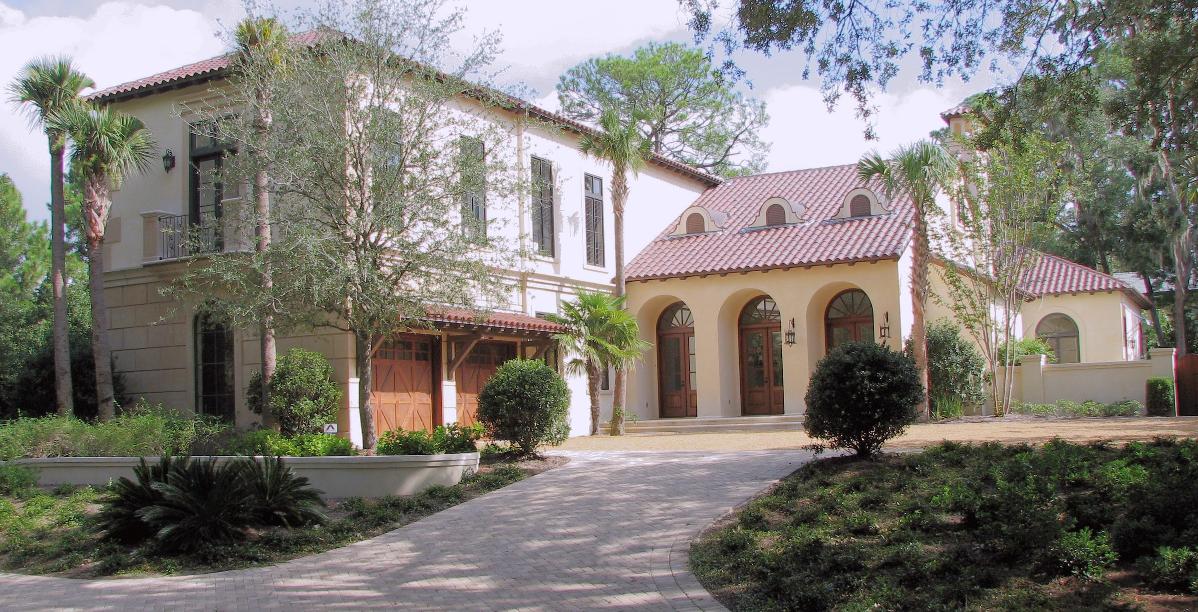 A coated residence with arched entries and palms, in full sun.